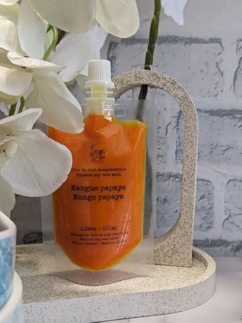 une bouteille de sirop de miel de mangue à côté d’une orchidée blanche