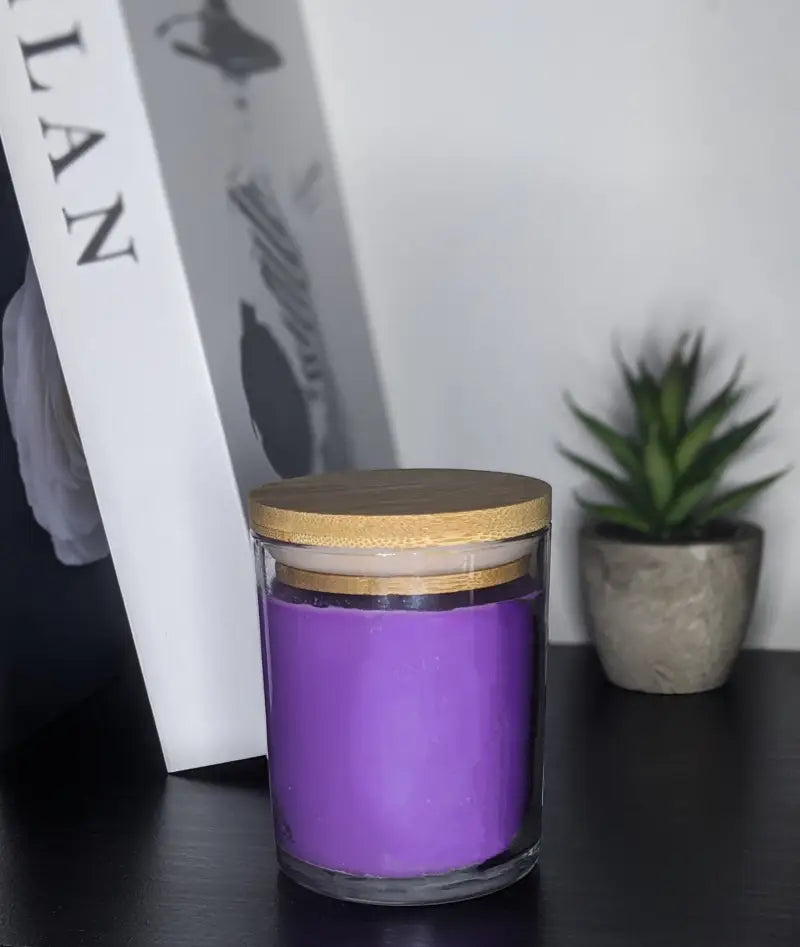 une bougie violette posée sur une table à côté d’une boîte blanche